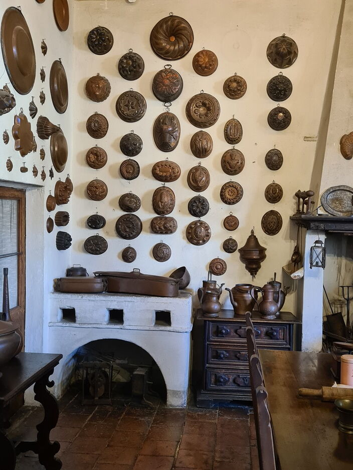 Foto einer historischen Küche mit Feuerstelle und zahlreichen Backformen an den Wänden